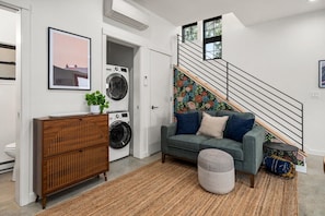 A modern living room with a sofa, ottoman, and a staircase. - Modern Home in Ballard | Workspace + EV Parking (Seattle)