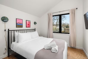 Un lit bien fait, avec du linge de lit blanc, une serviette enroulée et deux tableaux encadrés accrochés au mur.