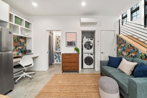 Un salon moderne comprenant un canapé, un bureau avec une chaise, un lave-linge et un escalier.