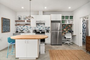 A modern kitchen with white cabinets, a stainless steel refrigerator, and a wooden island. - Modern Home in Ballard | Workspace + EV Parking (Seattle)