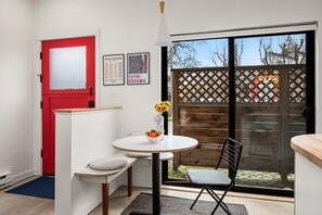 A compact room with a red door, a white wall, a small round table with a vase of flowers, a black chair, and a view through a sliding glass door to an outdoor area with a wooden fence. - Modern Home in Ballard | Workspace + EV Parking (Seattle)