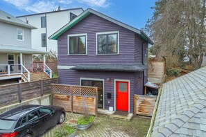 A two-story house with a red door, a garage, and a car parked in the driveway. - Modern Home in Ballard | Workspace + EV Parking (Seattle)