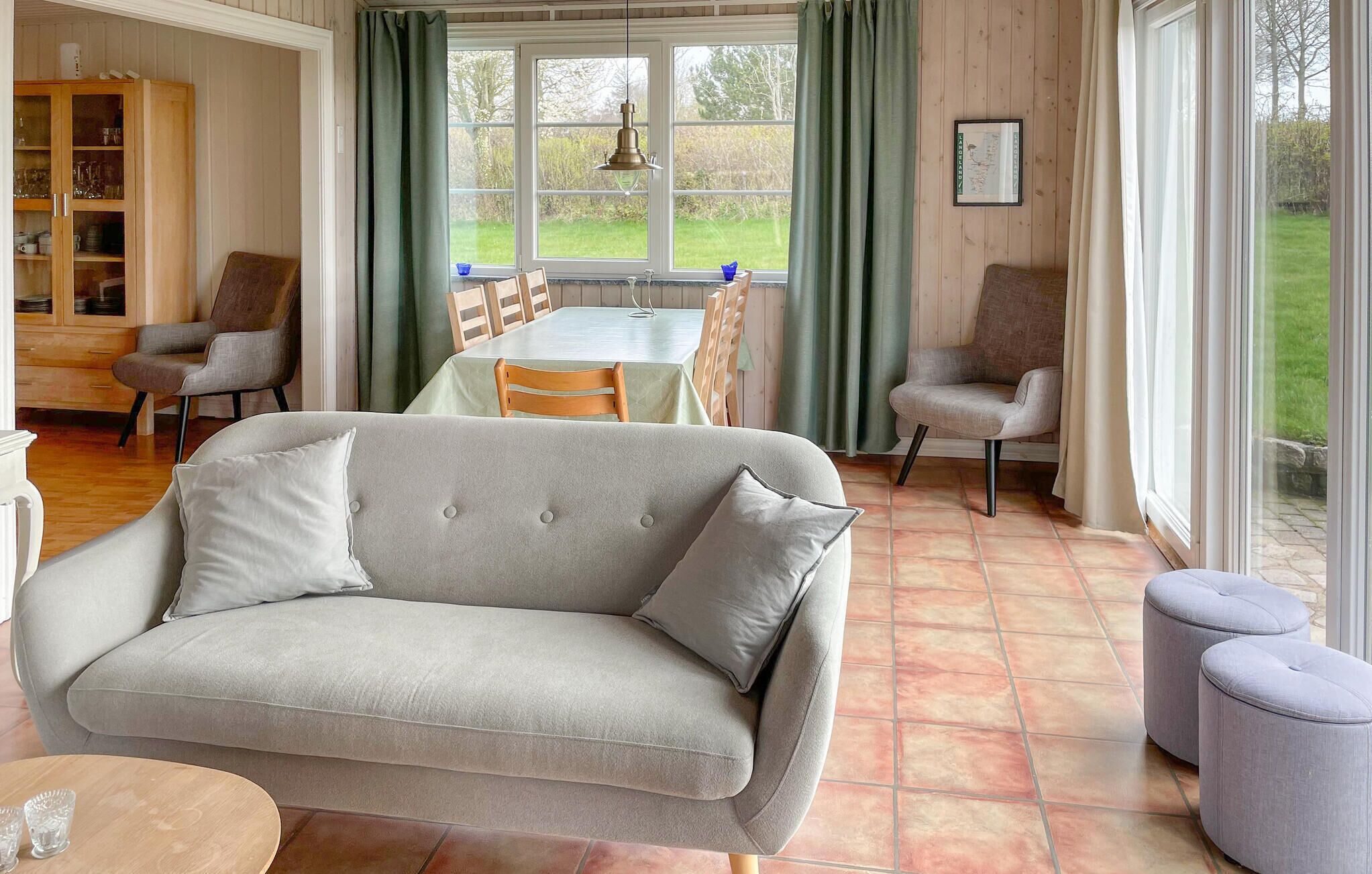 Ein Wohnzimmer mit einer Couch, Sesseln, einem Esstisch und Blick durch große Fenster.