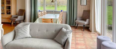 Ein Wohnzimmer mit einer Couch, Sesseln, einem Esstisch und Blick durch große Fenster.
