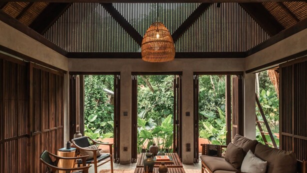 Una habitación con techo alto, ventanas amplias, una lámpara de fibra natural, un sofá, una mesa de centro y una silla.