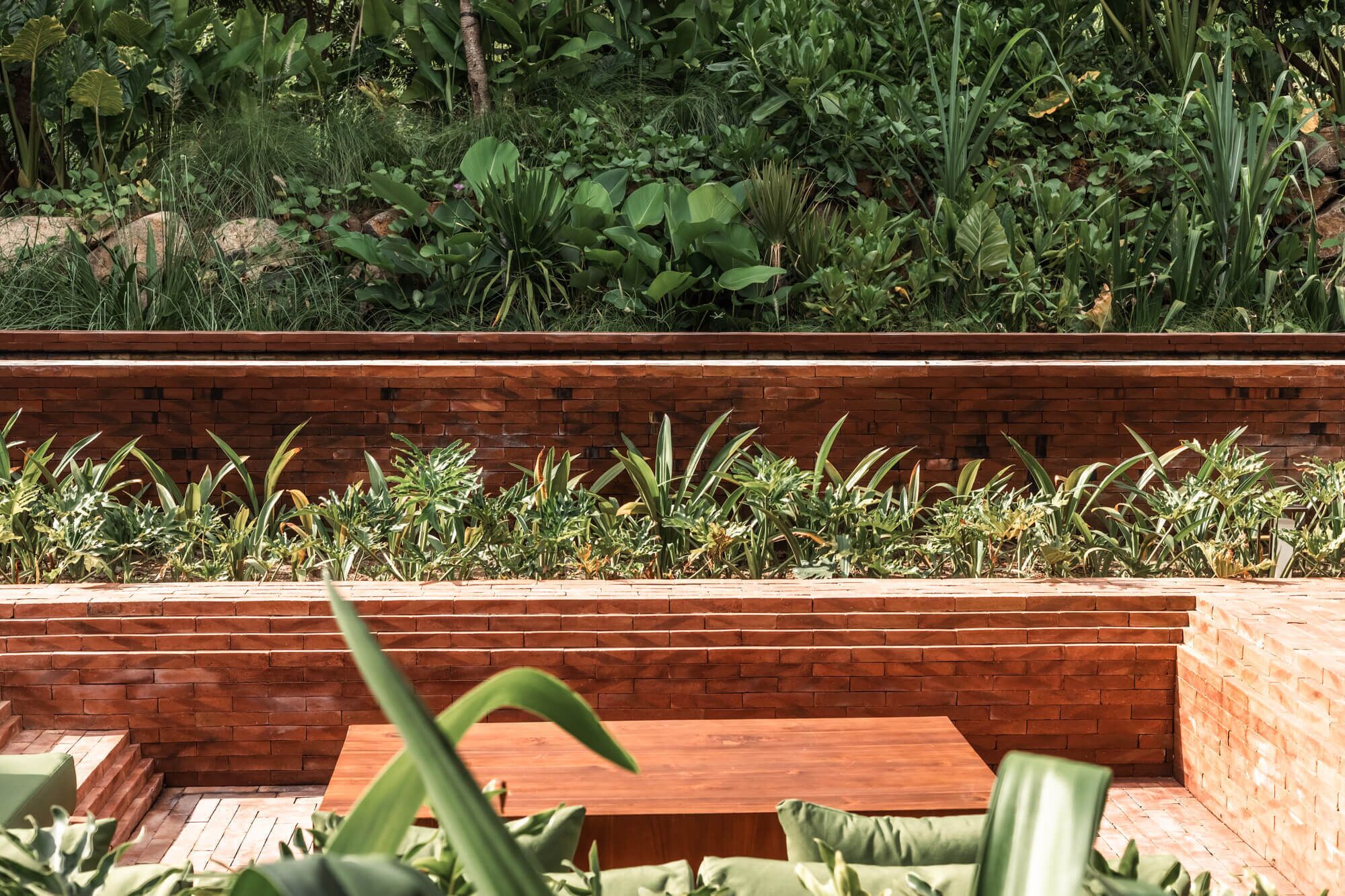 Jardín escalonado con muro de ladrillo, con diferentes plantas y un banco.