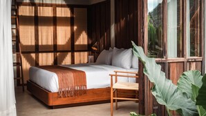 Un dormitorio con una cama de madera, una silla, una mesita de noche y un ventanal grande.