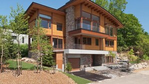 A two-story modern house with a stone facade, large windows, and a balcony.