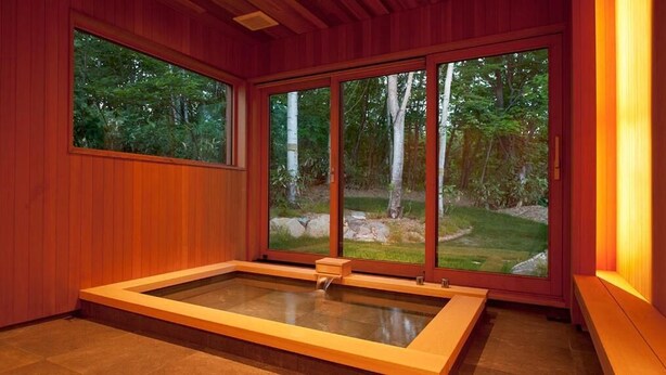 A spa room with a large window, a wooden floor, and a rectangular hot tub.