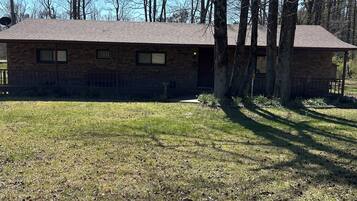 A single-story brick building with a sloped roof, surrounded by trees and a grassy yard.