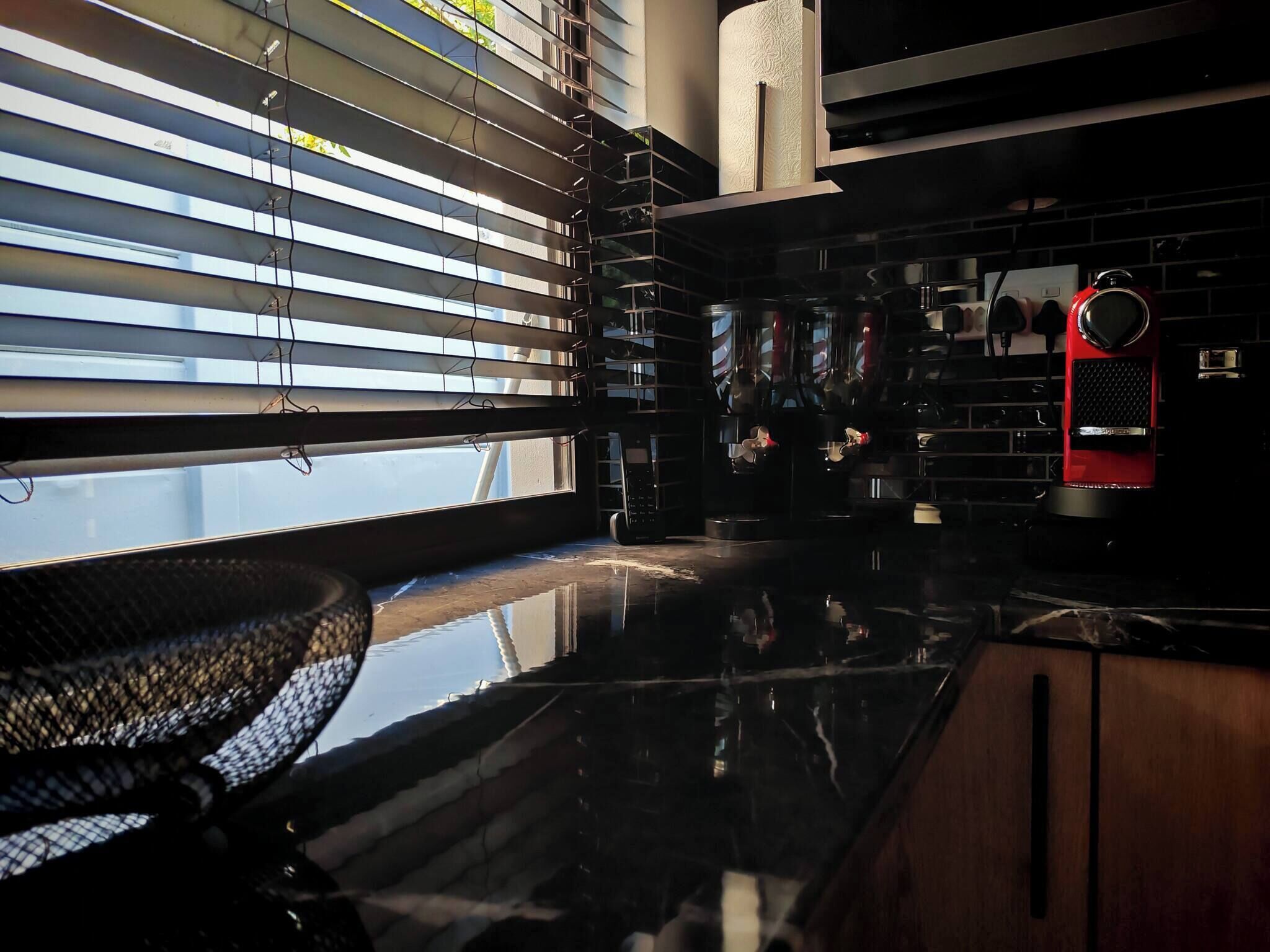 Una cocina moderna con encimera negra, electrodomésticos de acero inoxidable y un reloj rojo.