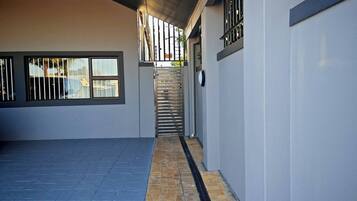 A covered outdoor area with a staircase leading to a higher level, a metal gate, and a paved floor.