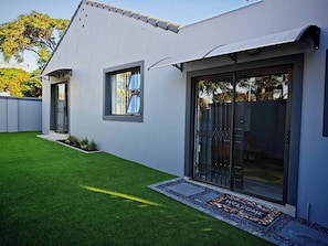 A modern house with a well-maintained lawn, a sliding glass door entrance, and a small porch area. - Room-courtyard Double Room With Shared B (Cape Town)