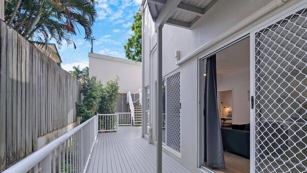 Een houten terras met een witte balustrade, een schuifdeur met hor en een trap naar een hoger gelegen niveau.