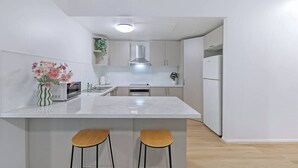 Een moderne keuken met een centraal eiland, twee barkrukken, een magnetron, een fornuis en een koelkast.
