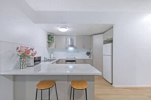 Eine moderne Küche mit einer zentralen Kochinsel, zwei Barhocker, einer Mikrowelle, einem Herd und einem Kühlschrank.