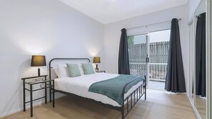 Een moderne slaapkamer met een metalen bedframe, witte beddengoed, twee bedlampjes en uitzicht op een balkon met gordijnen.