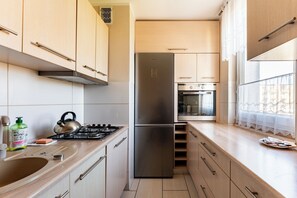 Eine moderne Küche mit Edelstahlgeräten, Holzschränken und einem Fenster mit Spitzenvorhängen.
