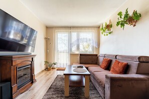 Ein Wohnzimmer mit Fernseher, Sofa, Holztisch und großen Fenstern.
