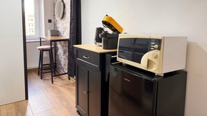Una cocina compacta con microondas, un refrigerador pequeño, una mesa de madera y una silla.