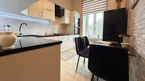 A modern kitchen with a central island, a dining area with chairs, and a large window with blinds. - Pułaskiego Spacious Apartment (Wrocław)