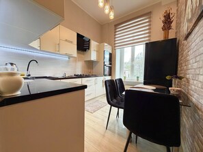 Eine moderne Küche mit einer zentralen Kochinsel, einem Essbereich mit Stühlen und einem großen Fenster mit Jalousien.