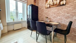A dining area with a brick wall, a window with blinds, a refrigerator, and a table with chairs. - Pułaskiego Spacious Apartment (Wrocław)