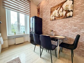 Ein Essbereich mit Backsteinwand, einem Fenster mit Jalousien, einem Kühlschrank und einem Tisch mit Stühlen.