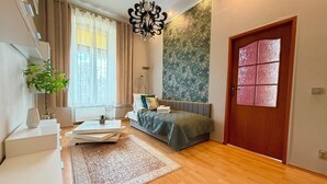 A modern bedroom with a bed, a desk, a chair, a plant, and a large window. - Pułaskiego Spacious Apartment (Wrocław)