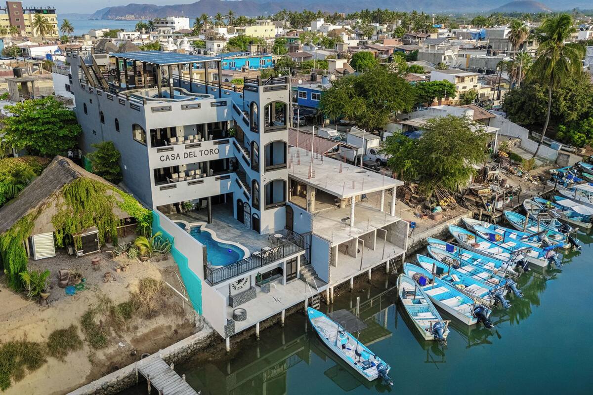 Un edificio de varios pisos llamado 'Casa Del Toro', con una piscina y barcos amarrados.