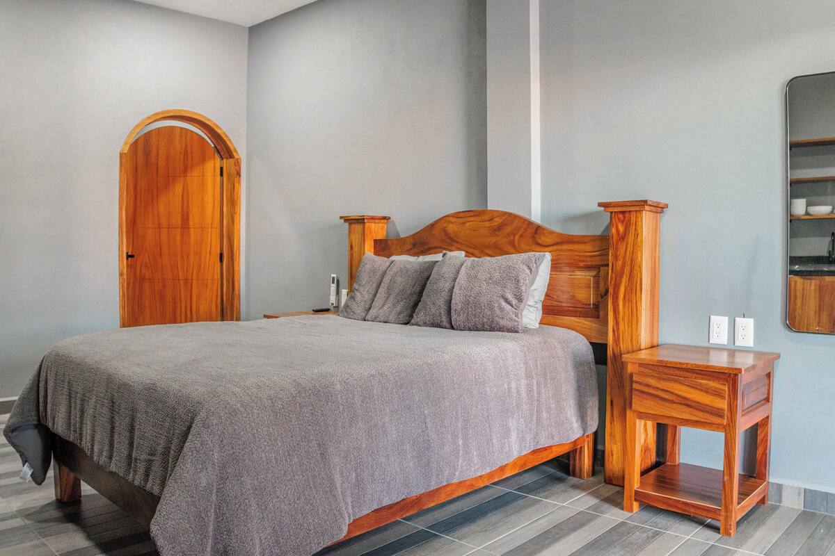 Un dormitorio con una cama de madera, una mesita de noche, un armario de madera y un espejo en la pared.