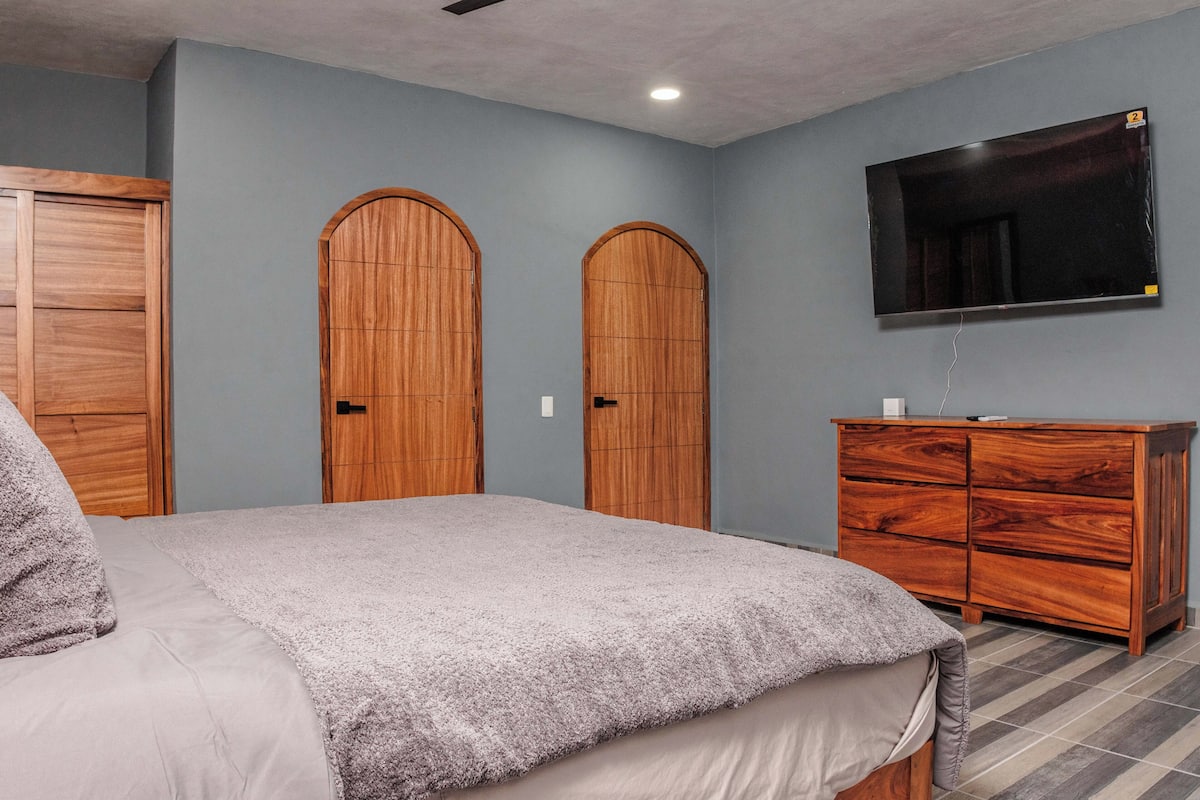 Un dormitorio con una cama, dos puertas de madera en arco, un televisor montado en la pared y un aparador de madera.