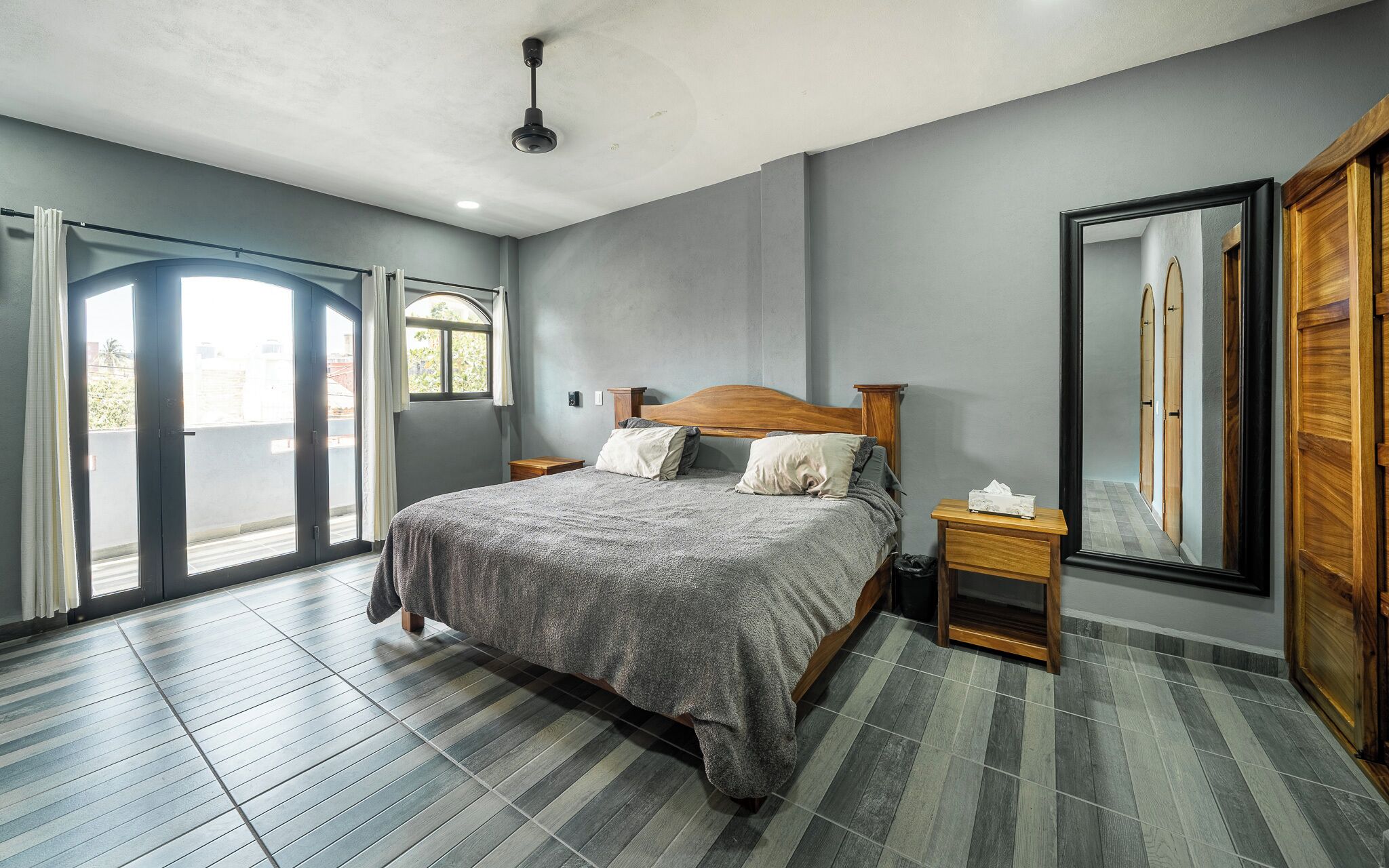 Un dormitorio con cama, mesita de noche, espejo y puerta corrediza a un balcón.