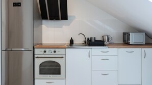 A compact kitchen with a refrigerator, oven, microwave, and a wooden countertop. - Sikorskiego Comfort Studio #4 (Rzeszów)