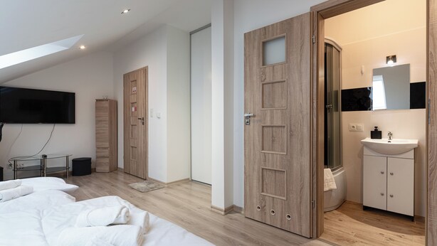 A modern bedroom with a large bed, a TV, a wooden wardrobe, and a bathroom with a mirror and sink. - Sikorskiego Comfort Studio #4 (Rzeszów)