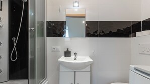 A modern bathroom with a glass-enclosed shower, a white sink with a mirror above it, and a toilet. - Sikorskiego Comfort Studio #4 (Rzeszów)