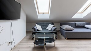 Ein modernes Schlafzimmer im Loftsstil mit Dachfenster, einem Flachbildfernseher, einem Glastisch und zwei Sofas.