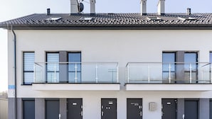 Ein modernes Gebäude mit Flachdach, zwei Balkonen mit Glasgeländern und einer Reihe von Türen.