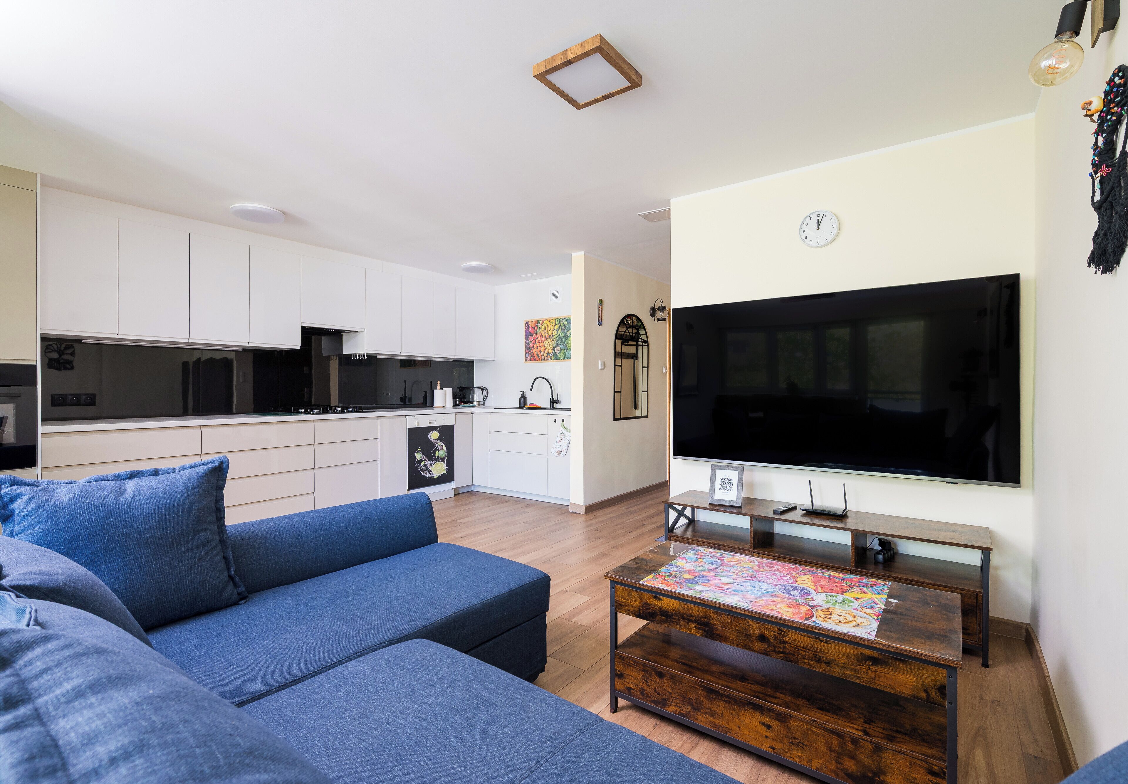 Ein modernes Wohnzimmer mit einer Couch, einem Couchtisch, einem Fernseher und einer Küche im Hintergrund.