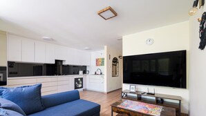 Ein modernes Wohnzimmer mit einer Couch, einem Couchtisch, einem Fernseher und einer Küche im Hintergrund.