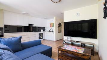 Ein modernes Wohnzimmer mit einer Couch, einem Couchtisch, einem Fernseher und einer Küche im Hintergrund.