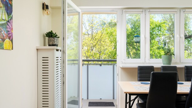 Ein Zimmer mit einer Schiebetür zum Balkon, einem Esstisch mit Stühlen, einem Blumentopf und einer wandmontierten Leuchte.