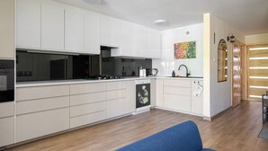 Eine moderne Küche mit weißen Schränken, einem Geschirrspüler und einem blauen Sofa im Wohnbereich.