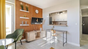 A modern living room with a TV, green chair, wooden cabinet, and a small table. - Park Śląski Charming Studio (Katowice)