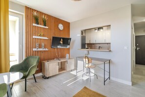 A modern living room with a TV, green chair, wooden cabinet, and a small table.