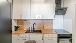 A modern kitchen with white cabinets, a wooden countertop, a stainless steel sink, and a built-in oven. - Park Śląski Charming Studio (Katowice)