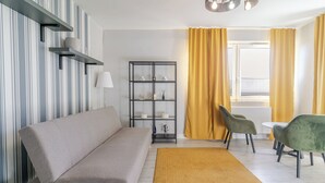 A living room with a sofa, a bookshelf, a table with chairs, and a yellow curtain. - Park Śląski Charming Studio (Katowice)