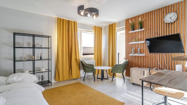 A modern hotel room with a bed, a desk, a TV, a bookshelf, and a dining area. - Park Śląski Charming Studio (Katowice)