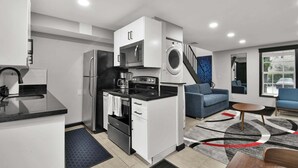Une cuisine compacte équipée d’un four à micro-ondes, d’un four et d’un lave-linge, ainsi qu’un canapé bleu et une petite table basse.