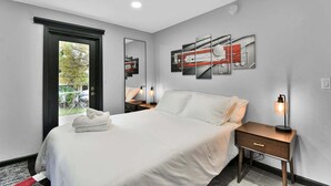 Une chambre moderne avec un grand lit, des tables de chevet, un miroir et des œuvres d’art abstraites accrochées au mur.